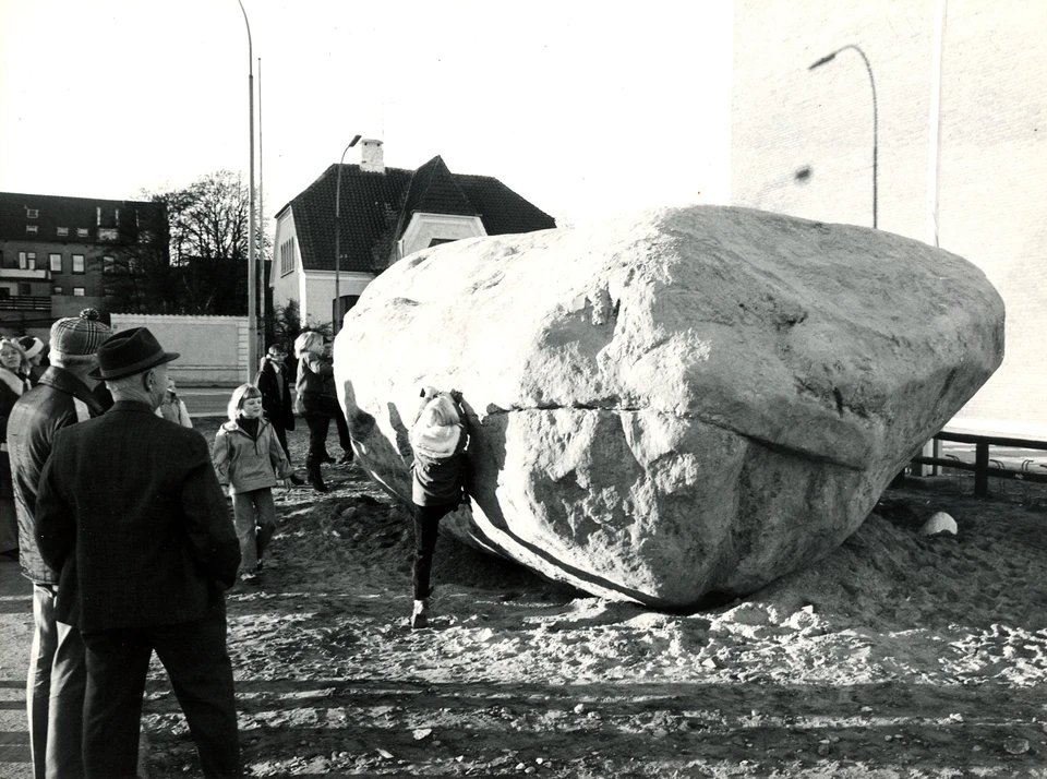 Et billede af kæmpestenen 'dynen' Foto: Henrik J. Granat Dynen Frederikshavnerne løftede i flok, da Dynen i 1975 blev hævet og lagt på plads ved det gamle Krudttårn. Dynen er en ledeblok af larvikit, der findes som fast fjeld omkring Larvik ved Oslofjorden. Den mægtige sten ved Krudttårnet i Frederikshavn har længe nydt æren som Jyllands andenstørste sten. Nye oplysninger og beregninger viser, at den må se sig degraderet til en fjerdeplads blandt de jyske kæmpesten.  Geologi Dynen består af bjergarten larvikit. Larvikit findes som faststående fjeld omkring Larvik ved Oslofjorden. Dynen er med andre ord en ledeblok, fordi vi kender udgangspunktet for rejsen, som indlandsisen tog den med på. Larvikit brydes og sælges som facadesten, bordplader og anvendes som smykkesten. Når lys brydes i feldspatkrystallernes tvillingelameller, fremkommer et blåligt perlemorsagtigt skær. Det kaldes at labradorisere.  Larvikit og rhombeporfyr er bror og søster blandt bjergarter. De har samme kemiske sammensætning, hvis man opløser dem til grundstoffer. Og de stammer fra samme vulkaner, der eksisterede i Karbon- og Permtiden for 300-700 mio. år siden. Men mens larvikitten størknede langsomt i dybet og udviklede store krystaller, boblede rhombeporfyren ovenud af vulkanen som lava og størknede langt hurtigere.  Larvikit består af op til 90% feldspatkrystaller, der er 2-4 cm store. Feldspat inddeles i hovedtyperne kalifeldspat med kalium og plagioklas med natrium og calcium. Larvikittens feldspat er helt særlig, idet den består af en blanding af de to typer og indeholder derfor både kalium, natrium og calcium. En sådan treholdig feldspat kaldes ternær.  Mellem feldspatkrystallerne findes et lille indhold af sorte mineraler, men ingen kvarts. Førhen klassificeredes bjergarten som en anorthoklas-syenit. I den nyeste internationale klassifikation henføres larvikit til bjergarten monzonit.  Larvikitstenene i Jylland Forbavsende mange af Nordjyllands og Midtjyllands store sten består af larvikit: Hundborgstenen i Thy, Nøvlingstenen og Gråstenen i Himmerland, og Troldestenen ved Biersted i Vendsyssel, samt mægtigst: Mørupstenen ved Herning, der anses for Jyllands største.  Stenens navn Dynen i Frederikshavn har en navnebror i Holckenhavns bugt syd for Nyborg. Navnet findes brugt på søkort om mudrede bløde grunde, men også om sten, der ballonagtigt hvælver sig op over vandspejlet. Den beskrivelse passer overordentlig godt på Frederikshavns Dynen, da den lå på lavt vand med kølen begravet i havbunden udfor Fladstrand, før det blev opfyldt.   Dynen i 1975 foran det nye posthus