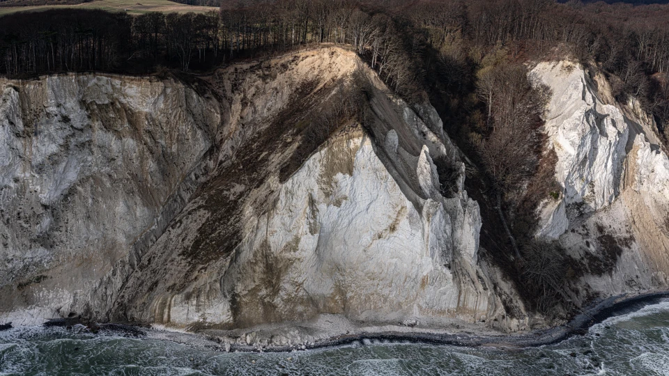 Møns Klint - en stor hvis og brunlig side rejser sig over et hav præget af bølger med skumtoppe.