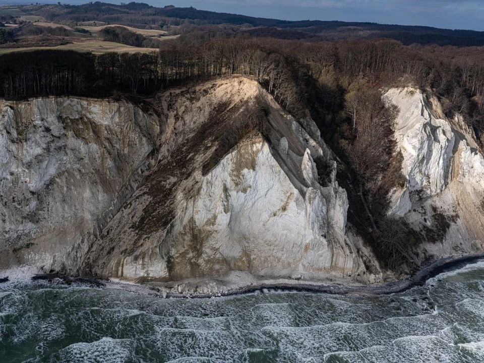 Møns Klint - en stor hvis og brunlig side rejser sig over et hav præget af bølger med skumtoppe.