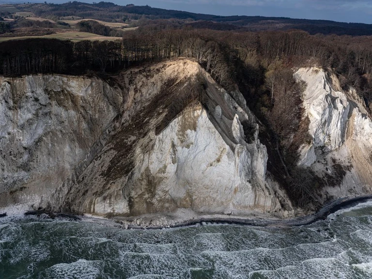 Møns Klint - en stor hvis og brunlig side rejser sig over et hav præget af bølger med skumtoppe.