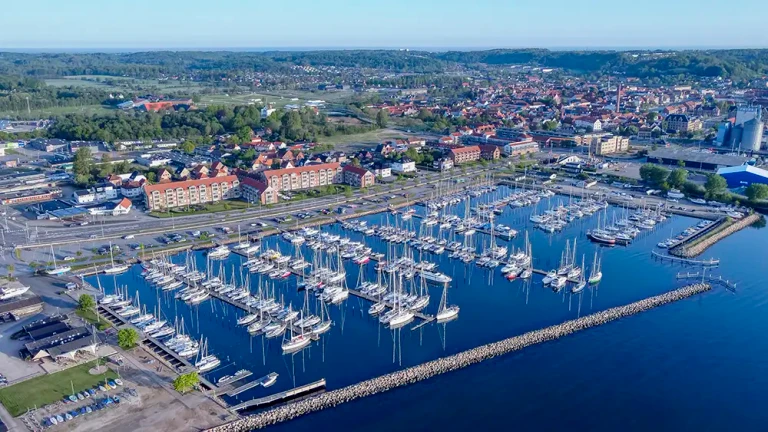 Kystbyen Aabenraa ses skråt fra oven med kig over en lystbådehavn og byen i baggrunden. I forgrunden ses havet.