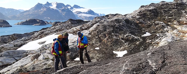 Tre mennesker med veste på, står på et bjerg