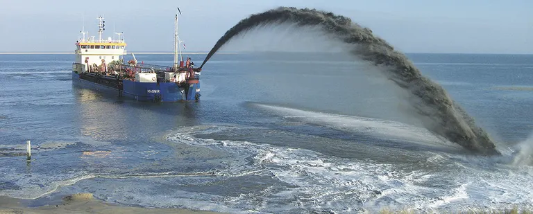 Sandsuger i færd med at tømme lasten i forbindelse med kystbeskyttelse af strandområde.
