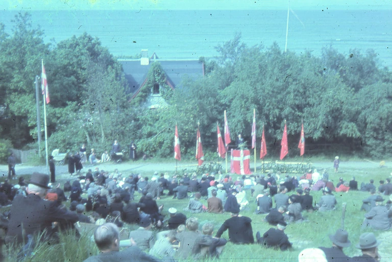 ( håndkoloreret) Selv om Alsang sluttede som en landsdækkende begivenhed i 1943, fortsatte man landet over med lokale alsangs- og algangsarrangementer. Her fra 5. maj 1945 i Strandbakkerne, Gilleleje, Fotograf Vilhelm Petersen.