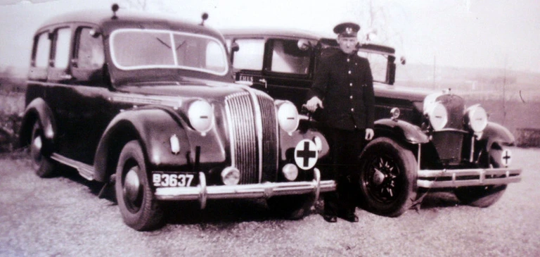 Præsentation af ny ambulance, Opel Admiral. Har ved indsættelsen overtaget nummerpladerne B 3637 fra den tidligere Nash-ambulance til højre, som formentlig da er udgået. Ambulancen har mørklagte forlygter, så det må være under besættelsen. Billedet er uden datering, men formentlig fra 1944-45. Udrykningslygter oppe på taget blev indført for udrykningskøretøjer i netop den periode. Ved ambulancen ses chauffør Bernhard Jacobsen.