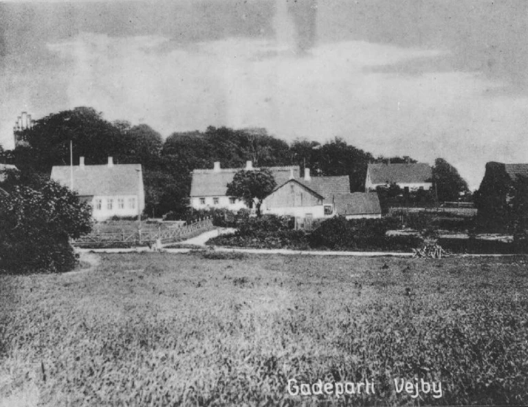 Et parti af Vejby omkring 1910. Midt i billedet ses rytterskolen, hvor Lars må have været elev som  barn. En rytterskole har umiddelbart ikke noget med ridning at gøre, selvom man kunne tro det. I  1720erne blev der bygget i alt 241 rytterskoler på krongodset, dvs. kongens jorder, til den lokale  almues børn. Krongodset var inddelt i rytterdistrikter, hvor alle bønderne i et enkelt rytterdistrikt  skulle brødføde en militær rytter og hans hest. Det var altså en form for skattebetaling, og skolerne  fik navn herefter. Fotograf ukendt.