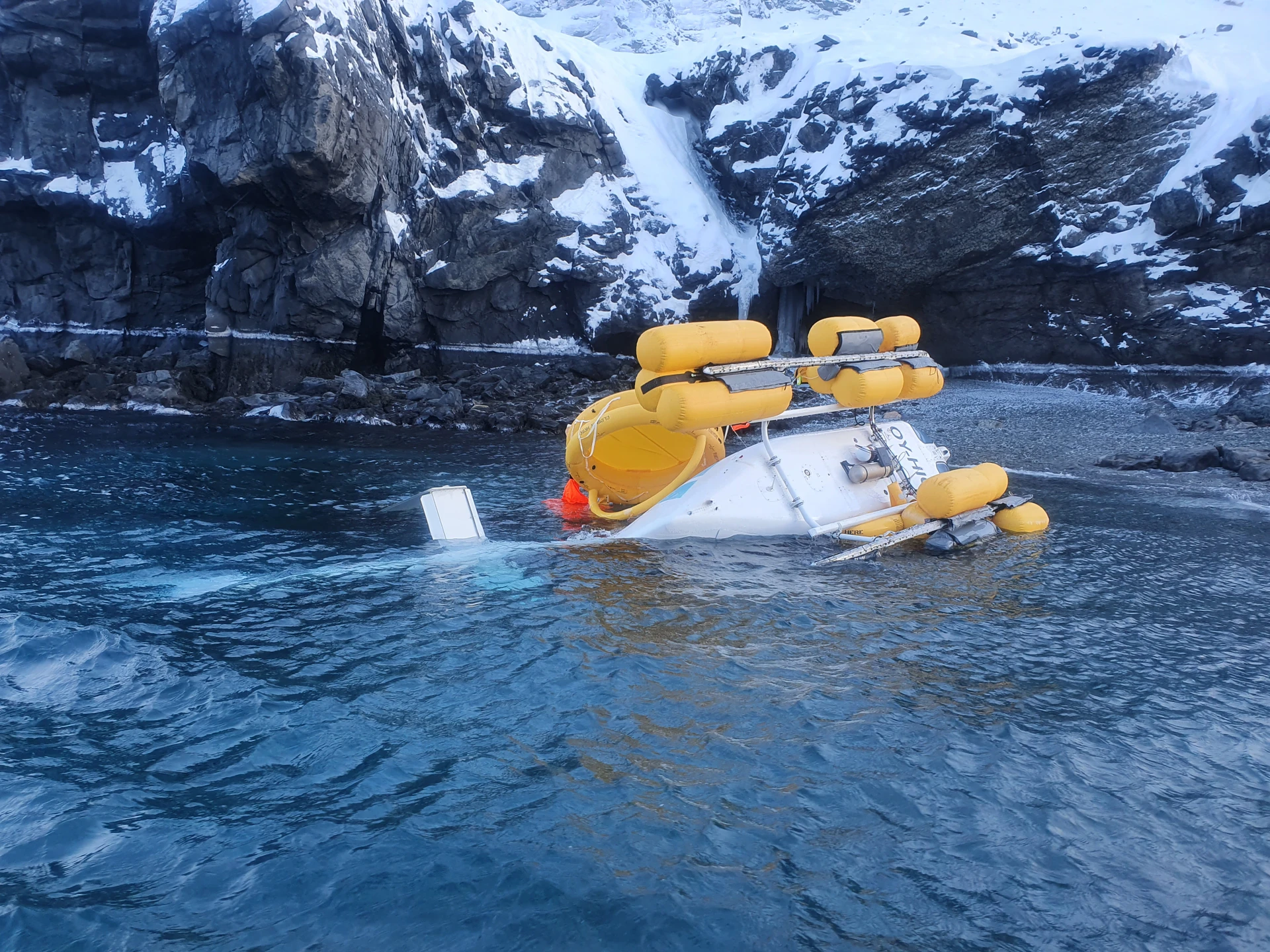 The helicopter on its LH side close to the shore