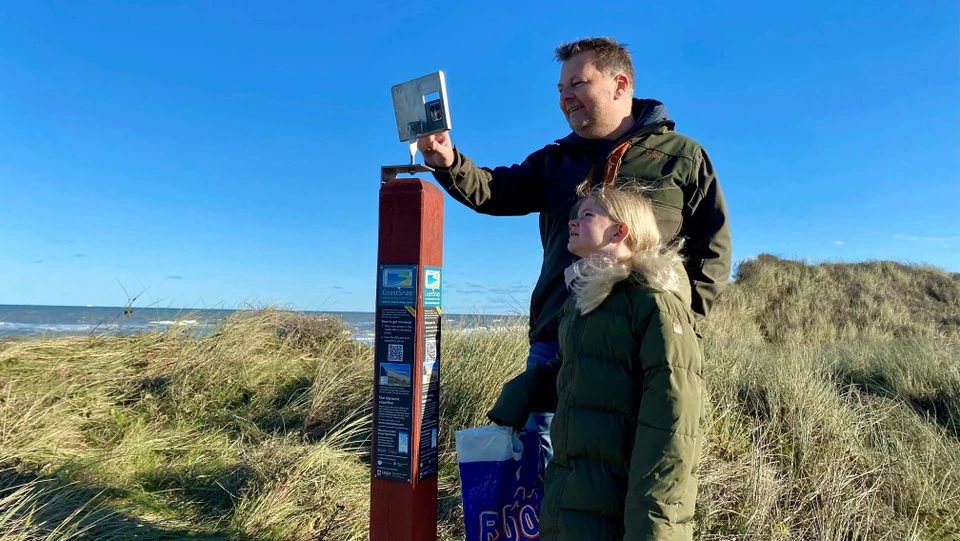 Billedet viser to personer som tager et foto med coastsnap holderen