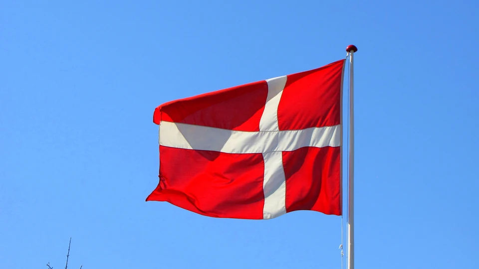 Dansk flag i flagstang foran en lyseblå himmel