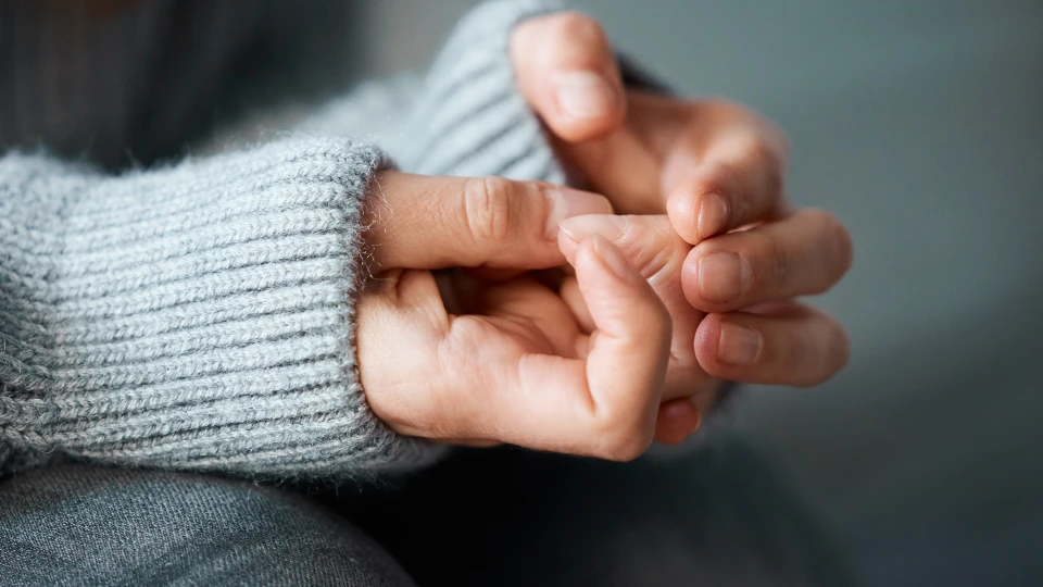 Knuede neglepillende kvindehænder stikker ud af nedtrukne sweaterærmer - udstråler bekymring og nervøsitet