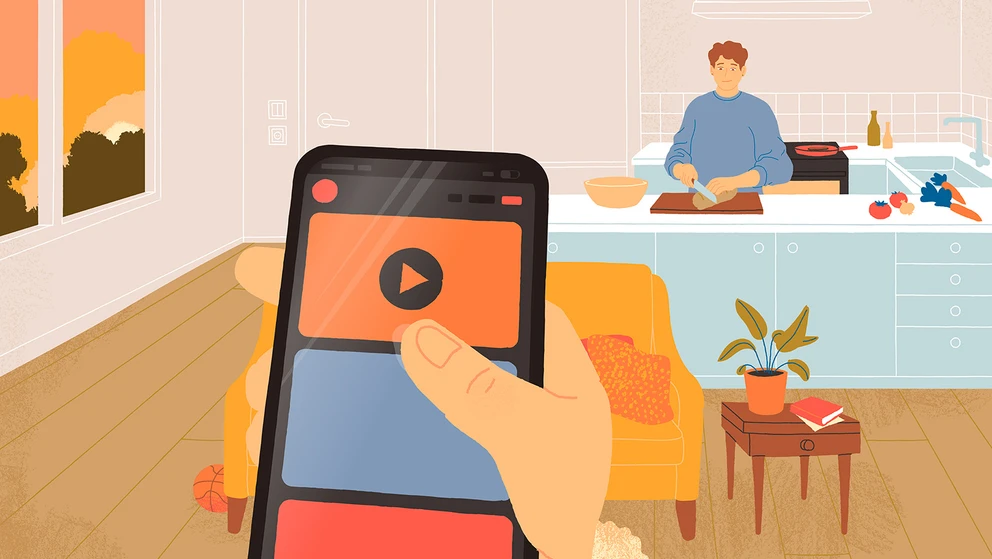 En hånd holder en telefon, mens en voksen laver mad i baggrunden.