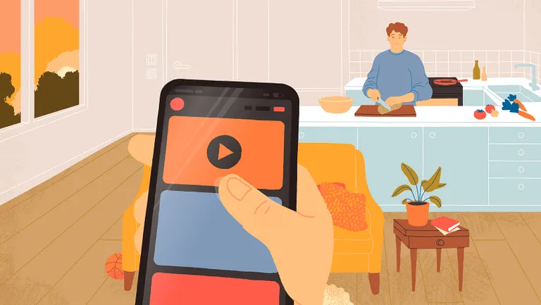 En hånd holder en telefon, mens en voksen laver mad i baggrunden.