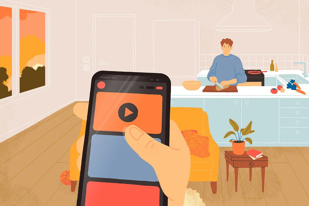 En hånd holder en telefon, mens en voksen laver mad i baggrunden.