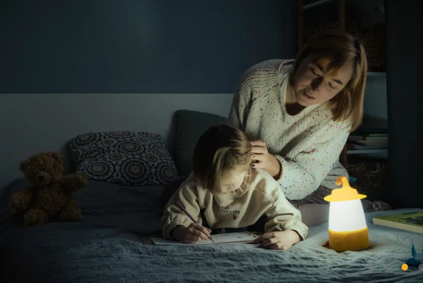 Mor og barn sidder og arbejder i skæret af en nødlampe