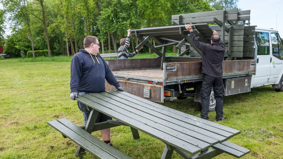Tre mænd bærer bordebænkesæt op på en ladvogn