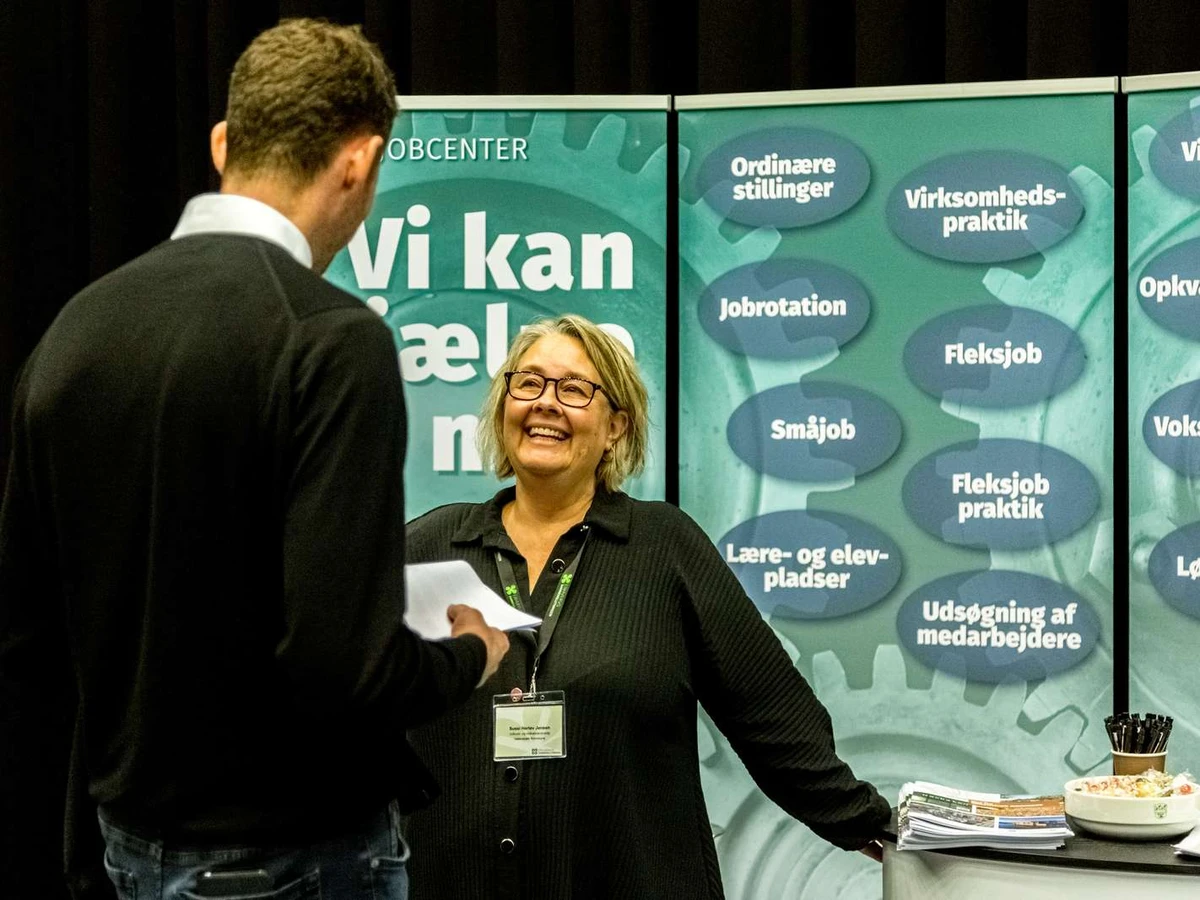 EN kvinde står i en stand og taler med en mand, der står med en blok.