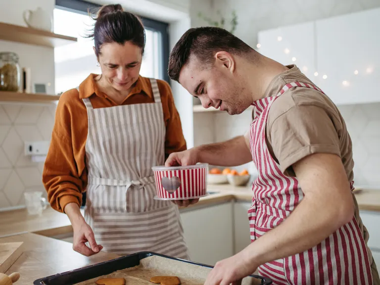 En kvinde og en ung mand står i køkkenet med forklæder henover en bageplade med småkager.