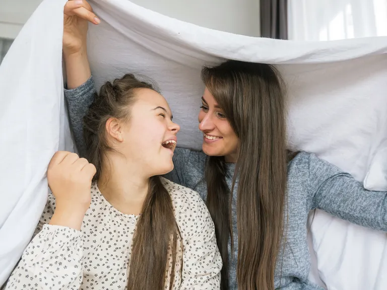 Ung kvinde med Downs syndrom og en middelaldrende kvinde holder et lagen over deres hoveder, imens de smiler til hinanden