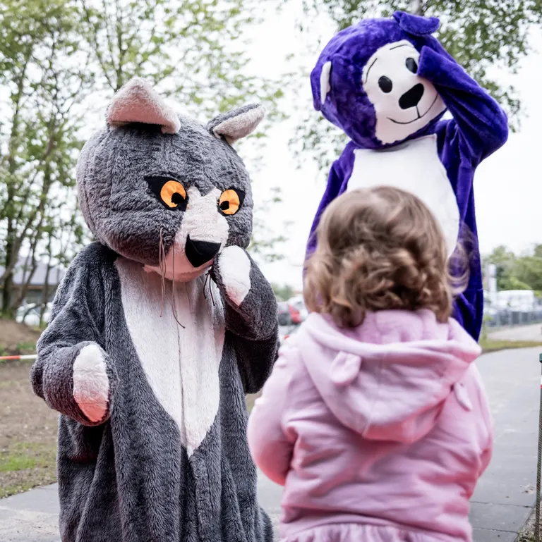 To voksne klædt ud som en mus og en bamse samt et barn med ryggen til kameraet